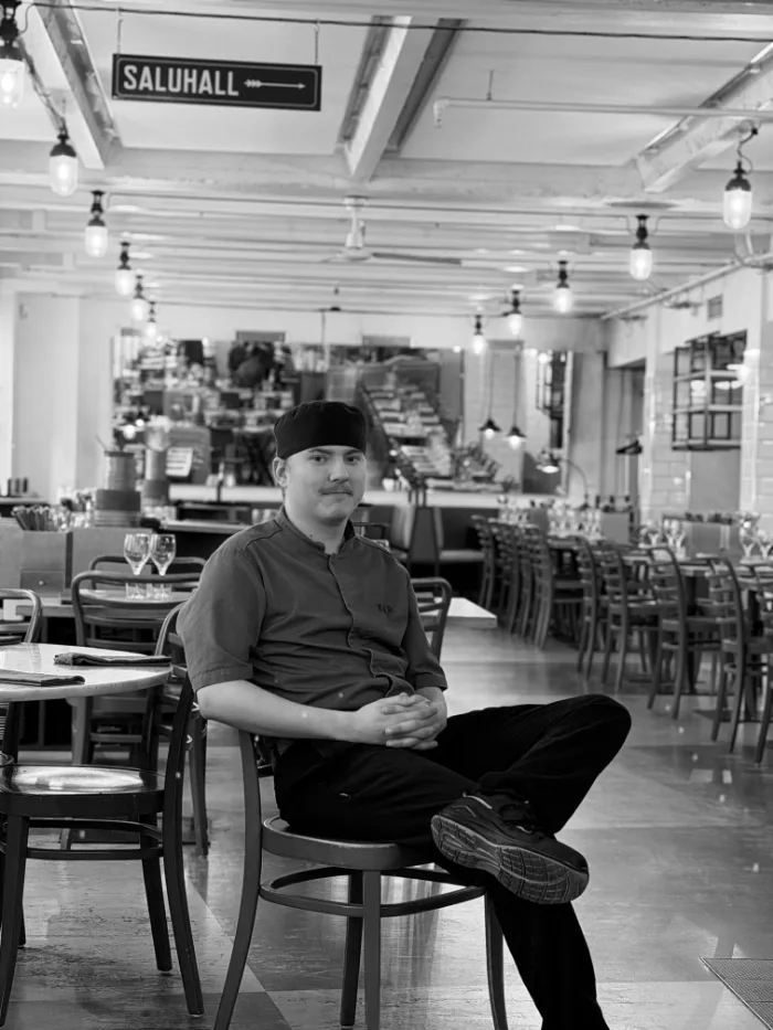 A member of the B.A.R. team in a dark shirt and a cap, seated in the dining room under the Saluhall sign