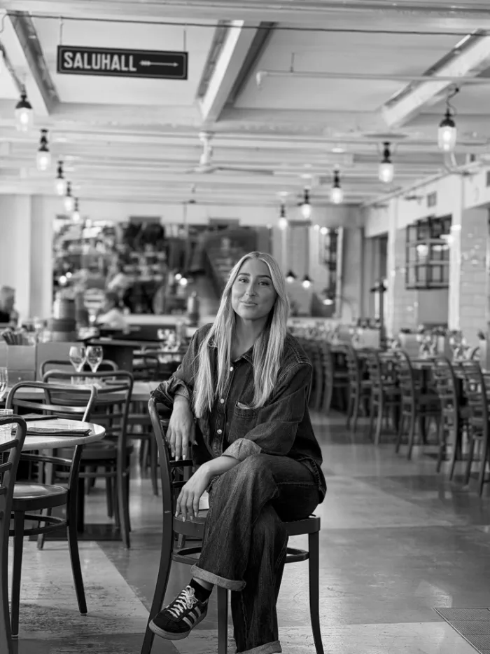 A member of the B.A.R. team in a dark shirt and long fair hair, seated in the dining room under the Saluhall sign