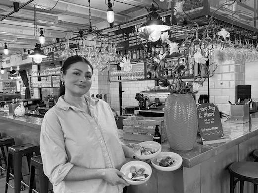 A server at the bar holding three small bowls of sides