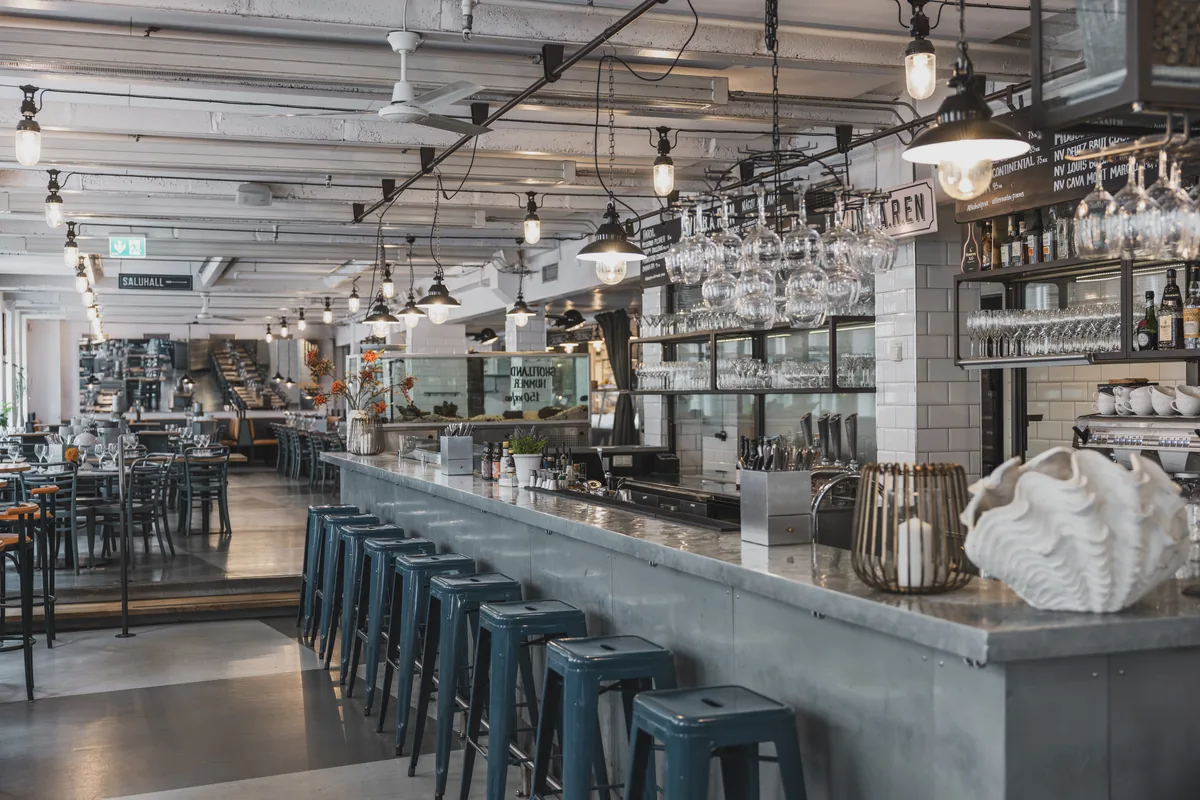 The concrete bar counter with blue bar stools, hanging glasses and the Baren sign under the ceiling