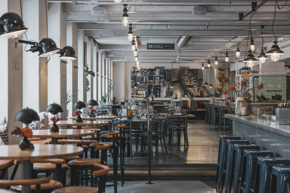The whole venue seen from the upper section: set tables, black lamps and the counter towards the market hall sign