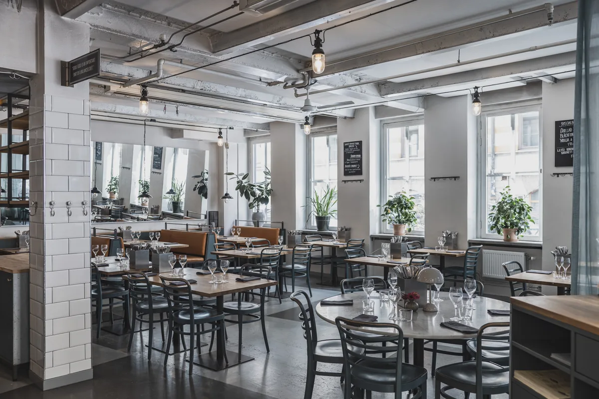 The lower dining room with set tables, bentwood chairs, leather benches and tall windows onto the street